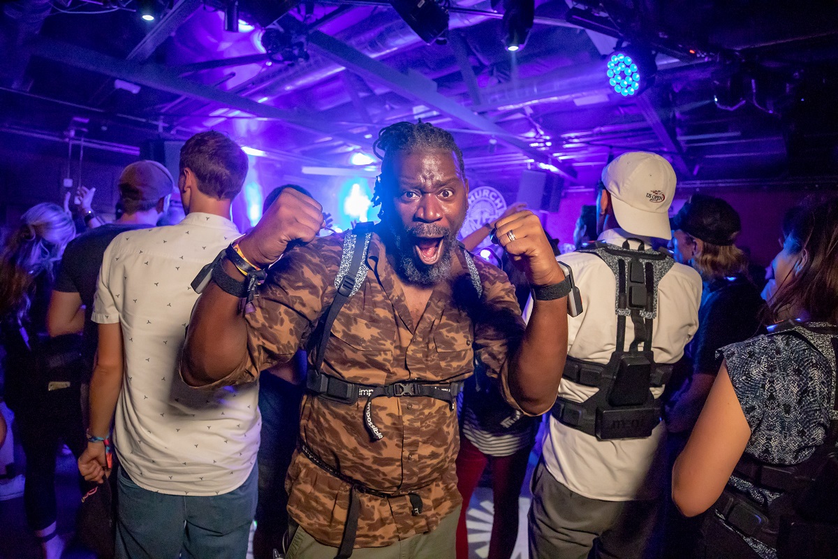 Using the Music: Not Impossible device African American man faces the camera with his mouth open, while a group of people behind him face the opposite direction