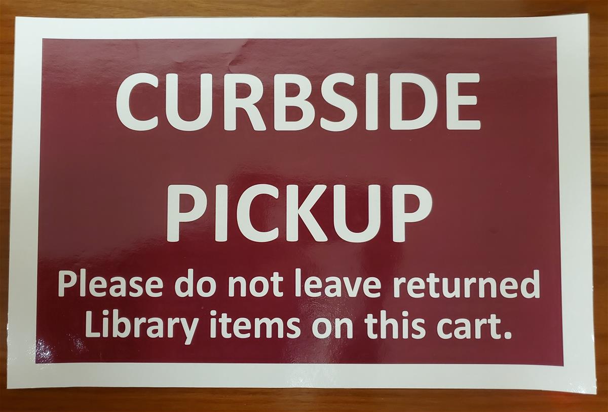 Maroon-colored sign with text "Curbside Pickup: Please do not leave returned library items on this cart."