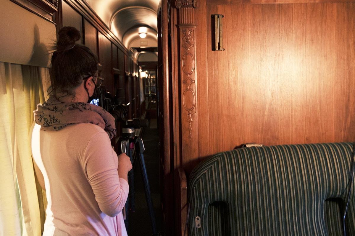 Digital Imaging Specialist Jillian Ferraiuolo setting up the shot of the Fair Lane railroad car hallway Back view of woman at camera on tripod pointing toward a narrow interior hallway