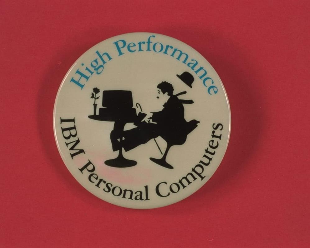 Advertising Button for IBM Personal Computers, circa 1985 White button with silhouette image of Charlie Chaplin sitting in a chair that appears to be falling backwards at a table that holds a computer and vase of flowers; also contains text