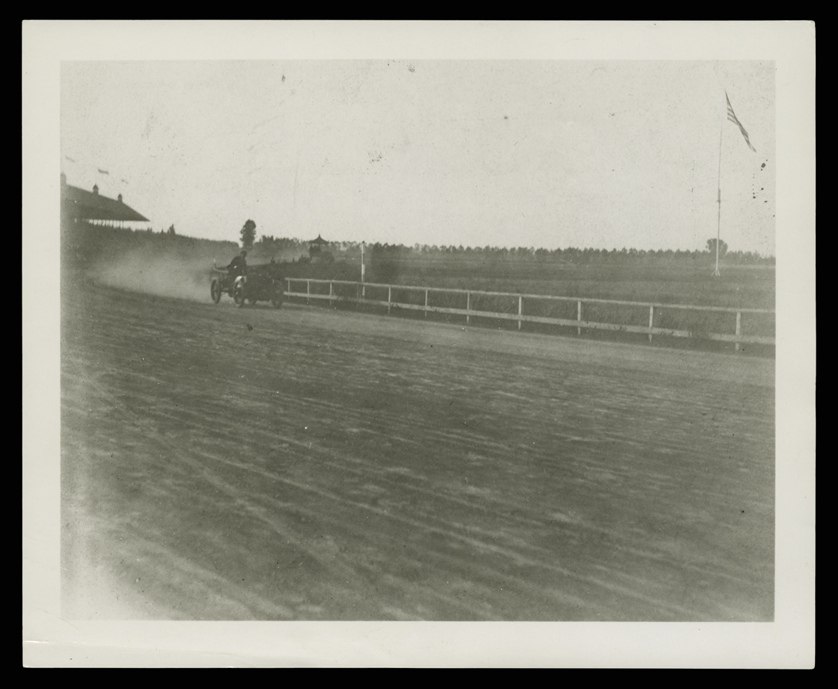 Henry Ford and Ed (Spider) Huff Driving the Ford Sweepstakes Racer at Grosse Pointe, Michigan, October 10, 1901 Early minimal race car in the mid-distance on a dirt track with a fence and grass behind it