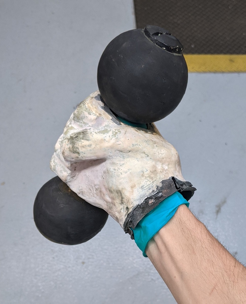 The size of the fist Person's wrist wearing blue glove inside white sculpted fist holding a barbell