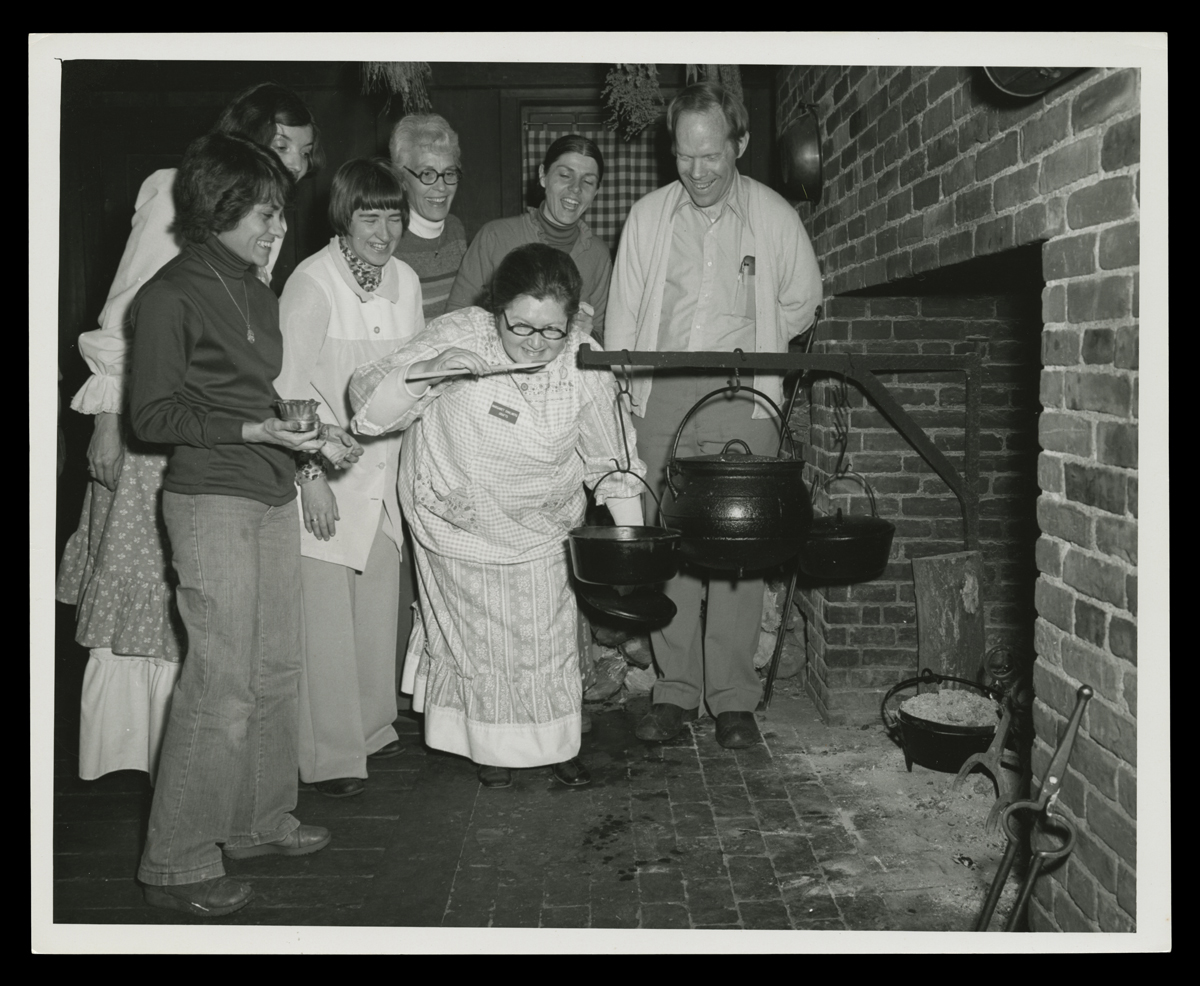 Group of people gathered around a fireplace and a cauldron on a swing arm