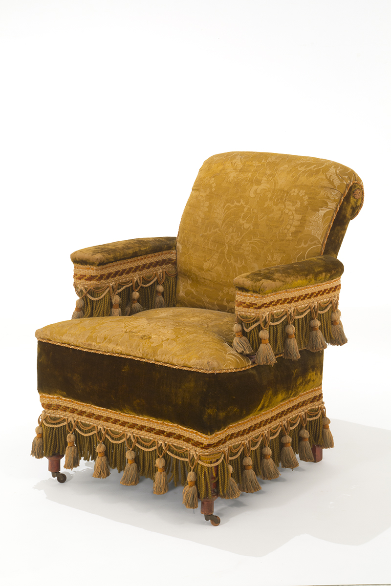 Upholstered yellow chair with multiple types of fabric, decorated with many large tassels
