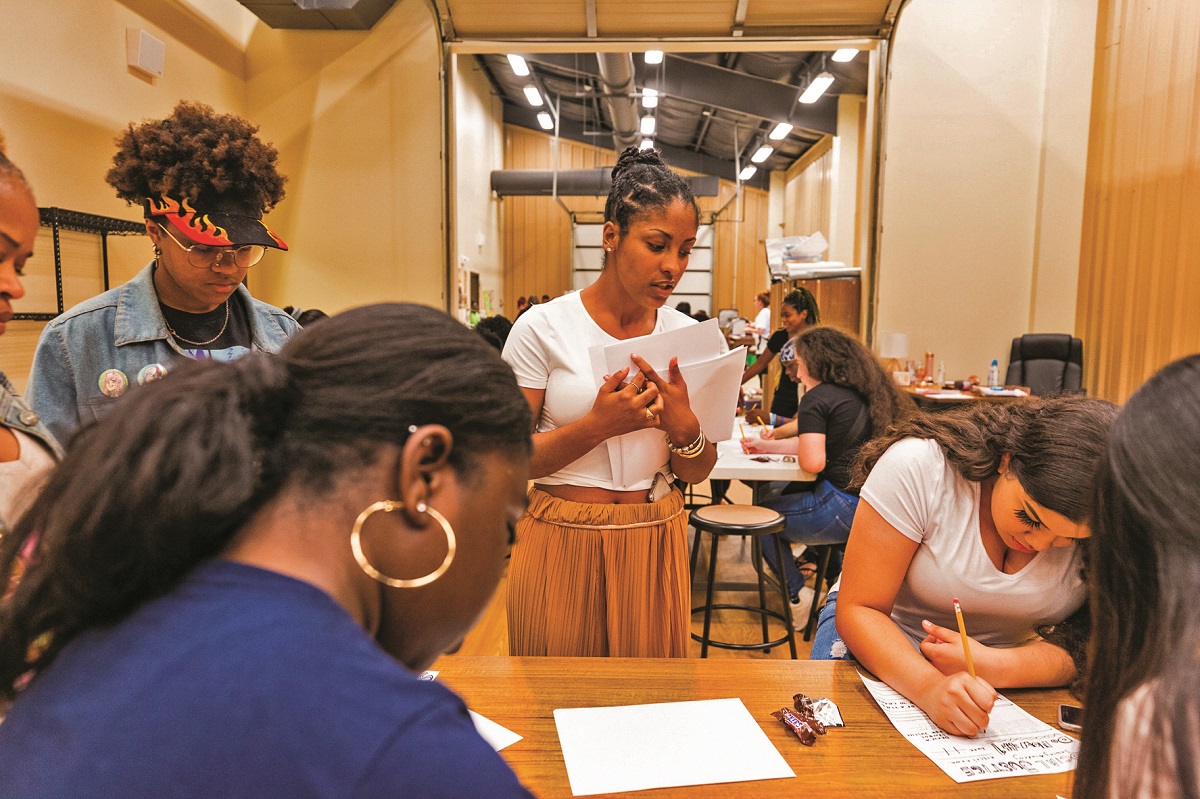 Sara Trail oversees a workshop at a Memphis high school A group of young people write on paper around a table, with other groups working at other tables in the background