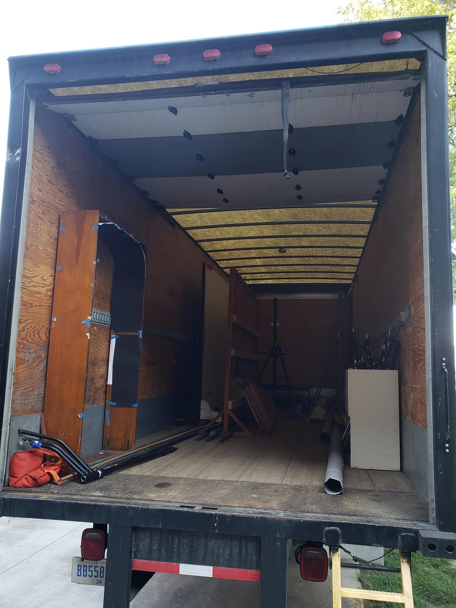 Open back of box truck containing some furniture and equipment