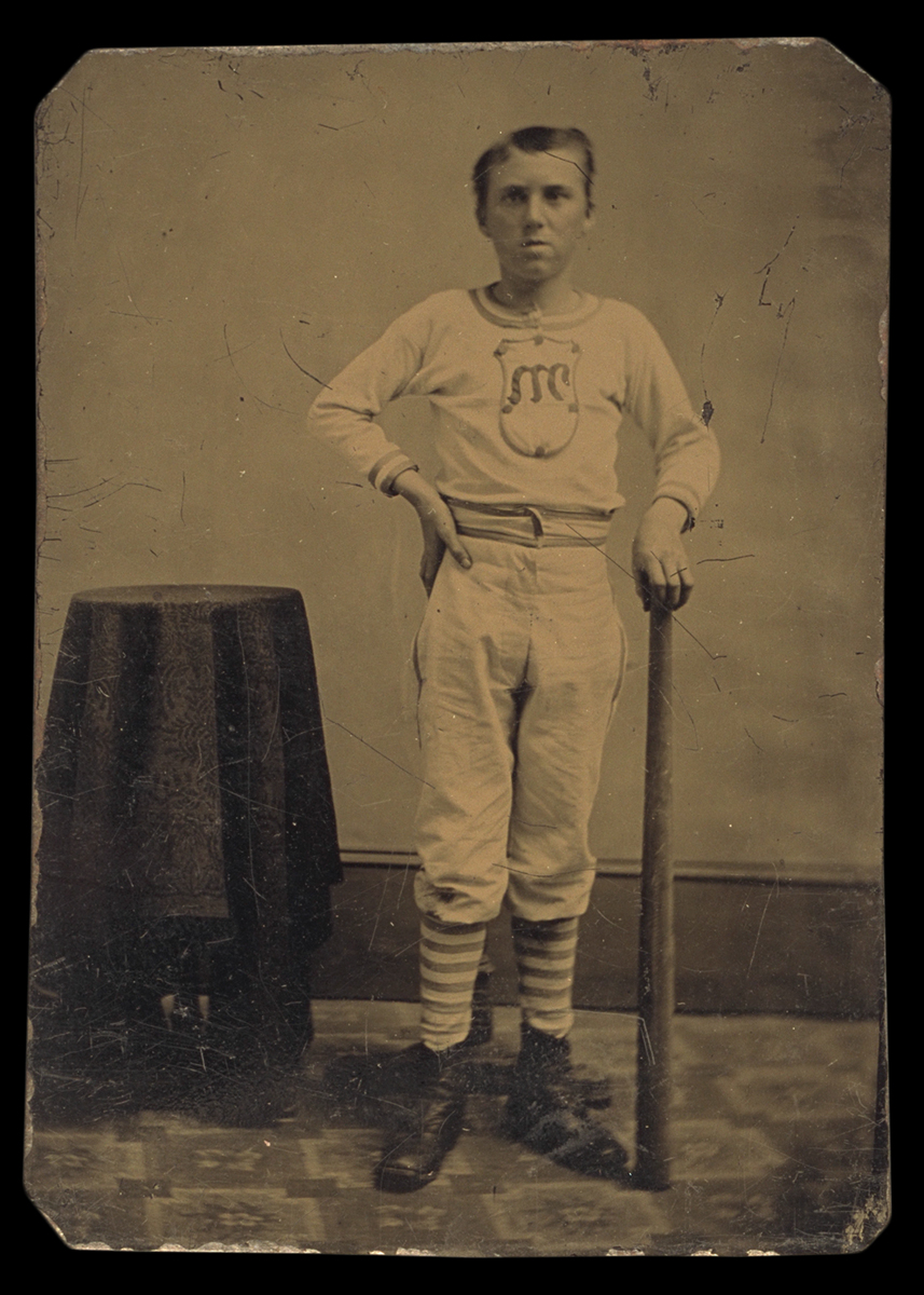 Man in baseball clothes holding bat, standing next to small table