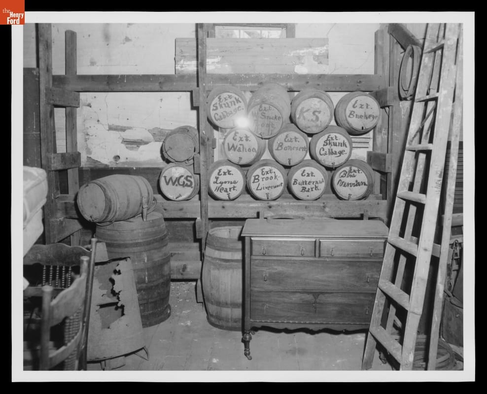 Dr. Howard's Office, Original Site, Tekonsha, Michigan, 1956 Black-and-white photo of storage room containing casks on racks, barrels, and furniture