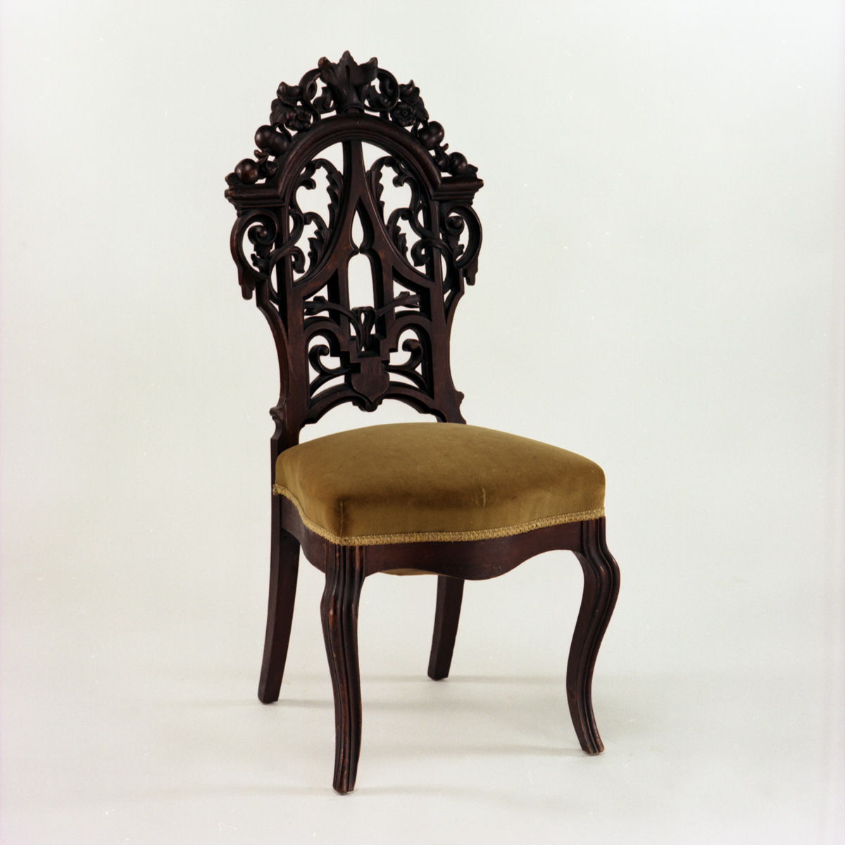 Chair with mustard yellow velvet seat cushion and intricately carved dark wood back