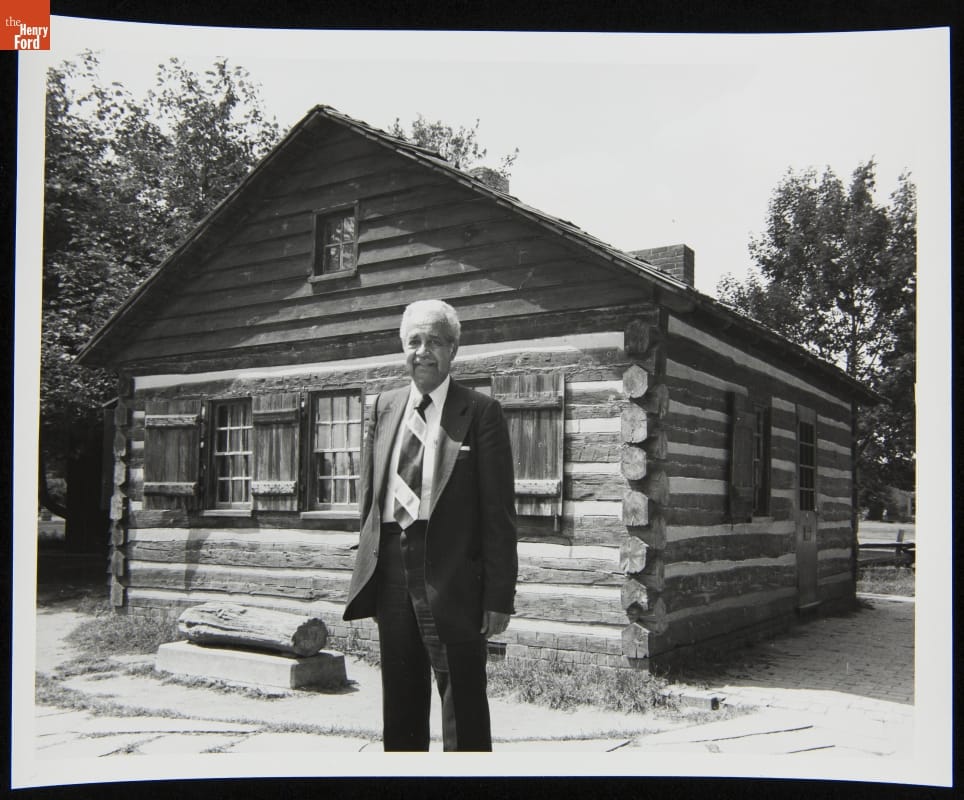 Austin W. Curtis Visiting the George Washington Carver Cabin in Greenfield Village, August 17, 1982 Black-and-white photo of man in suit standing in front of small wooden cabin