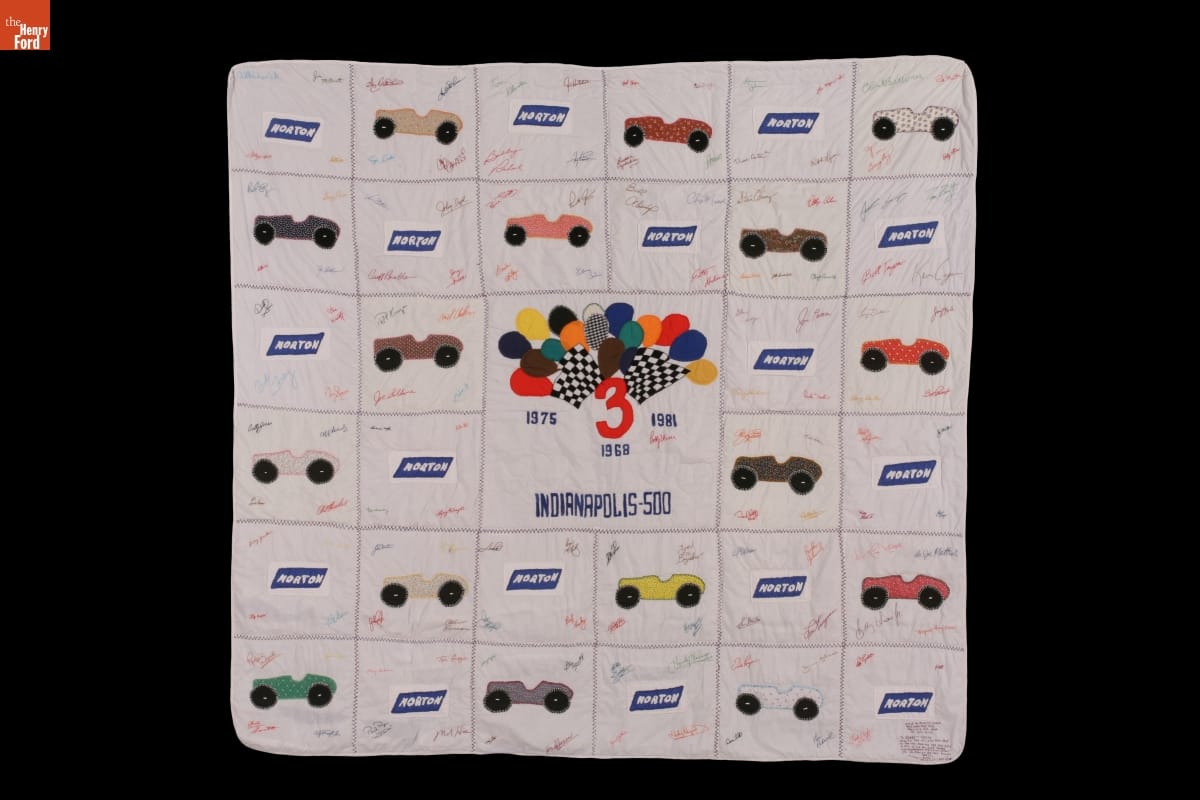 Quilt with blocks alternately featuring cars and logo for "Norton," along with balloons and checkered flags in the middle and signatures throughout