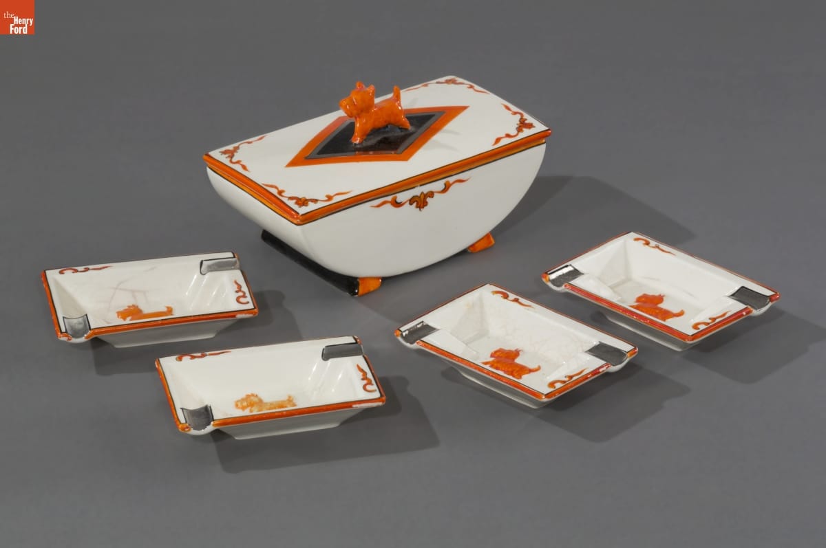 "Scottie Dog" Cigarette Holder and Ash Trays, 1935-1940 White arc-shaped dish with orange decorations and an orange Scottie dog on top, sitting with four small rectangular dishes with orange Scottie dogs inside the bottom