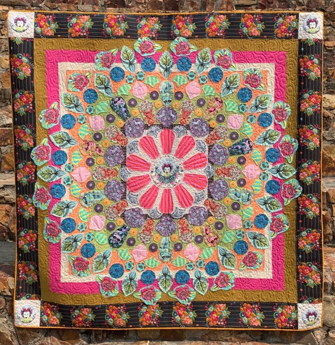 Tula Pink Millefiori, Kristin Barrus, 2017. Multicolored quilt with pink flower in the center of concentric design