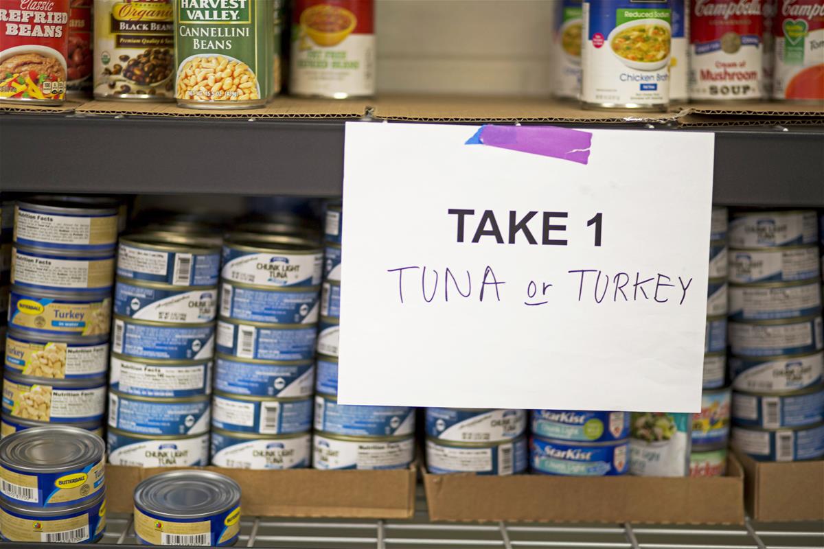 Canned good offerings Shelves with cans of tuna, turkey, and vegetables, with sign reading "Take 1: Tuna or Turkey"