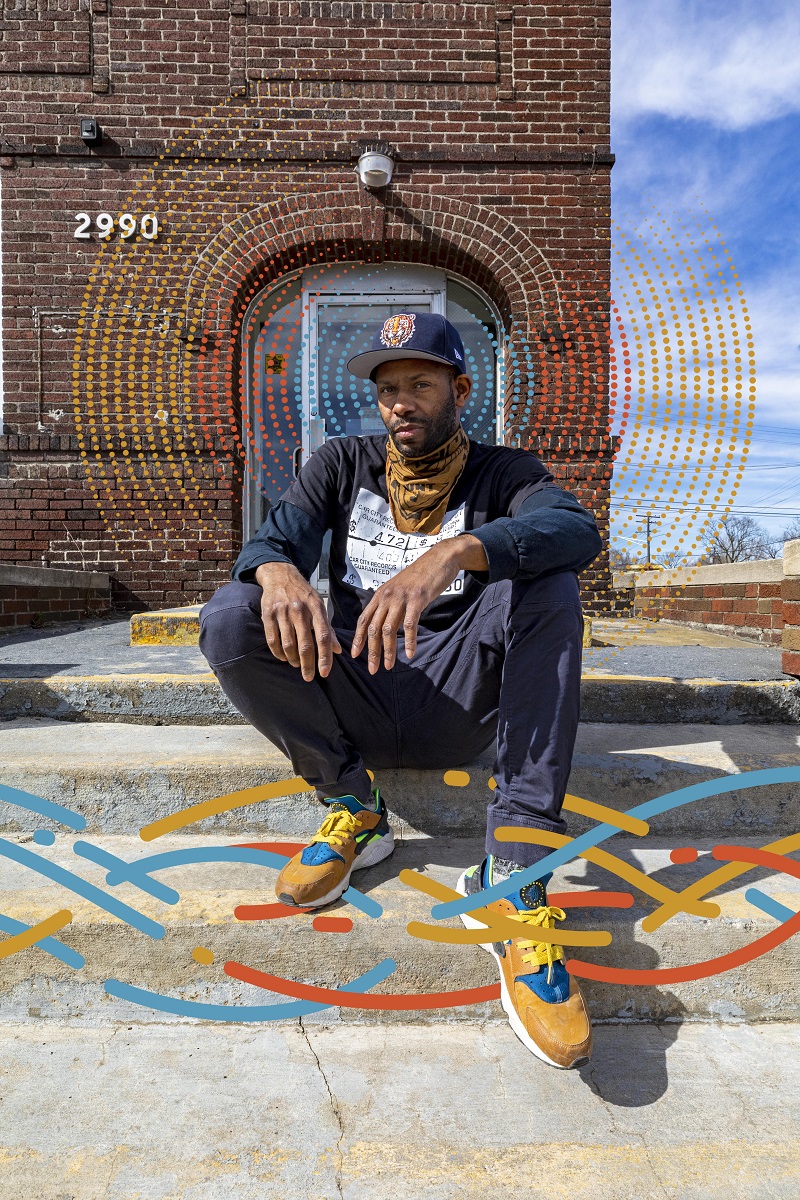 Waajeed on the steps of the future Underground Music Academy African American man sits on steps outside a red brick building; a colorful graphic of wavy lines has been added to the photo