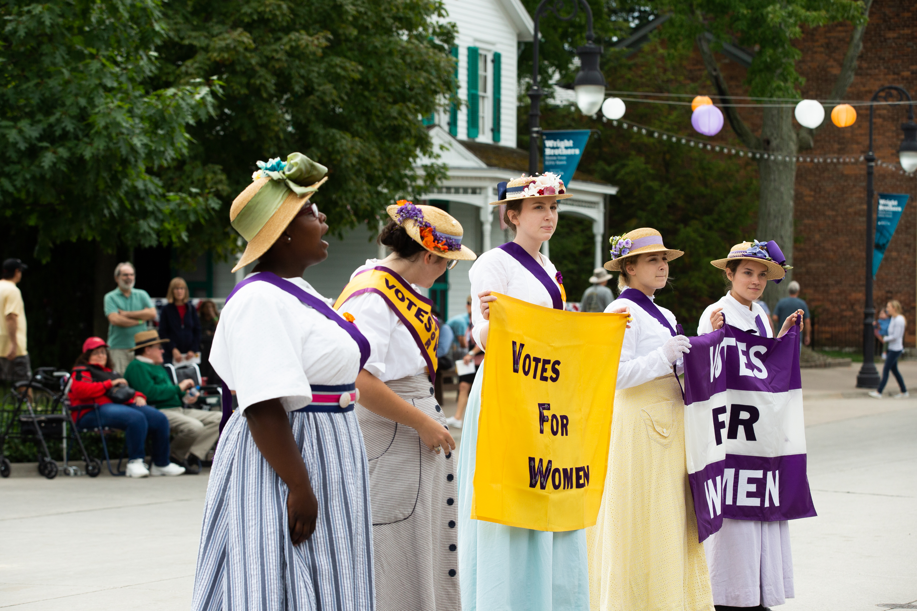 Five women wearing sashes and holding signs related to women's suffrage