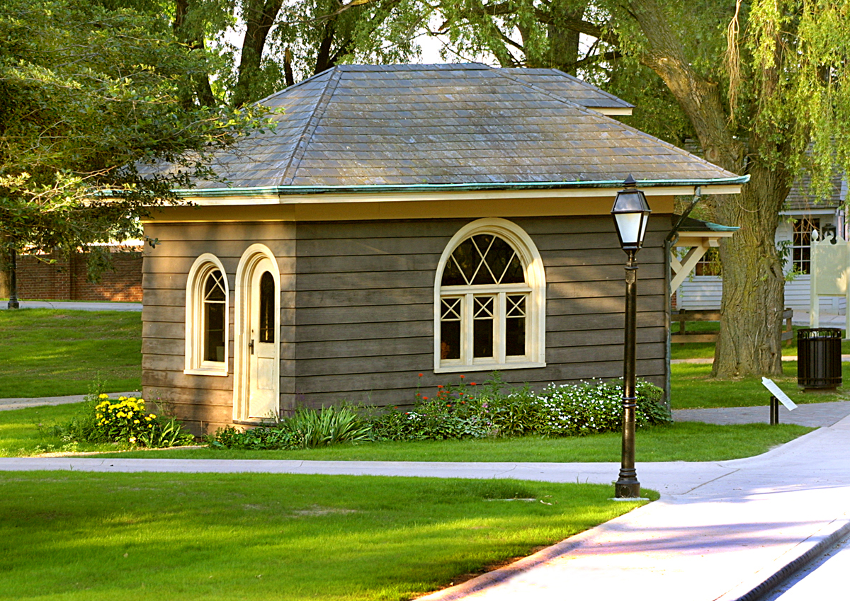 Small gray wooden building with arched windows and door