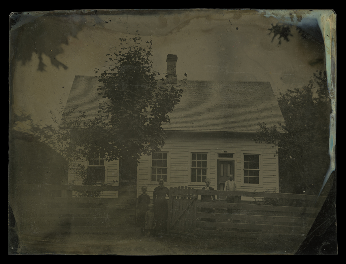 People standing behind fence and at gate in front of wooden house