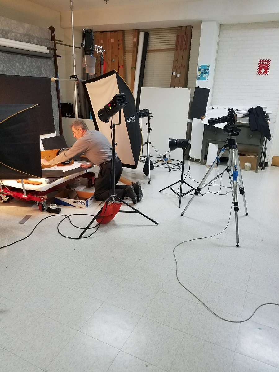 Man kneels and arranges a photo set with lights and camera pointing at it