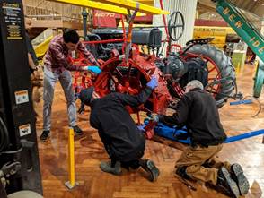 Installing the metal wheels Three men stand and kneel around a piece of equipment, holding a red metal tire