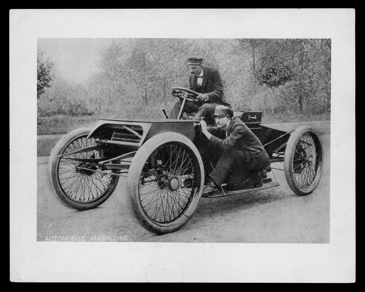 Henry Ford and Spider Huff with the Sweepstakes Racer on a Detroit, Michigan Street, 1901 Man sits in early open race car, with another man crouching on running board