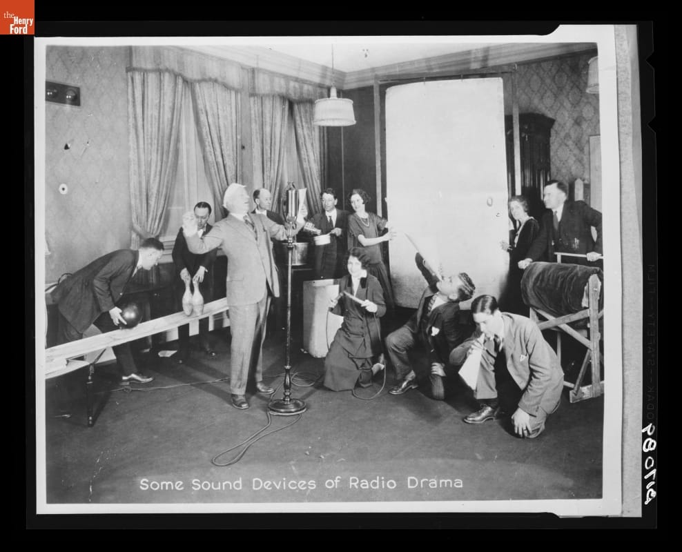 Behind the Scenes of a Radio Drama, 1923 Man at a microphone is surrounded by many people with various noise-making items