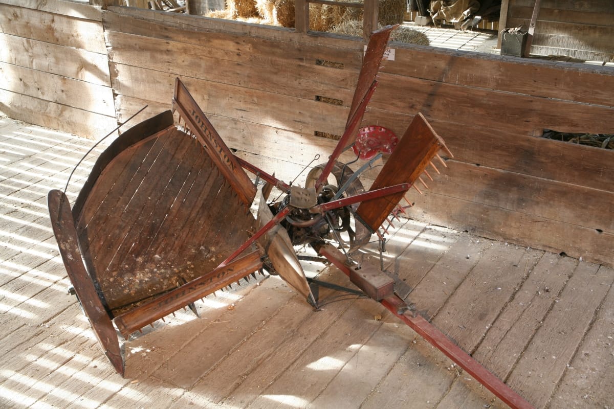 Johnston Harvester Co. Self-Rake Reaper, 1878-1900 Piece of large farm equipment, with wooden platform, long wooden beam, and toothed wooden rakes, sitting in wooden barn