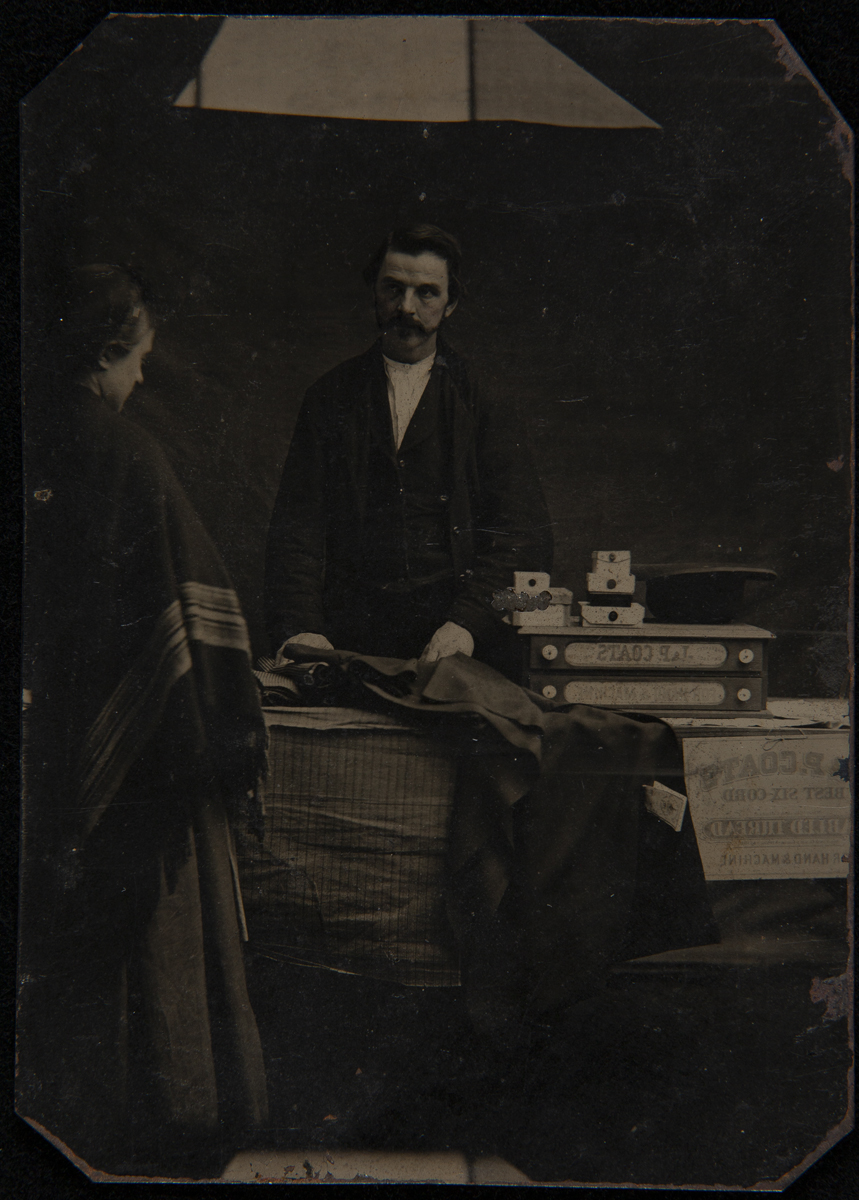 Man behind table containing products while woman looks at them
