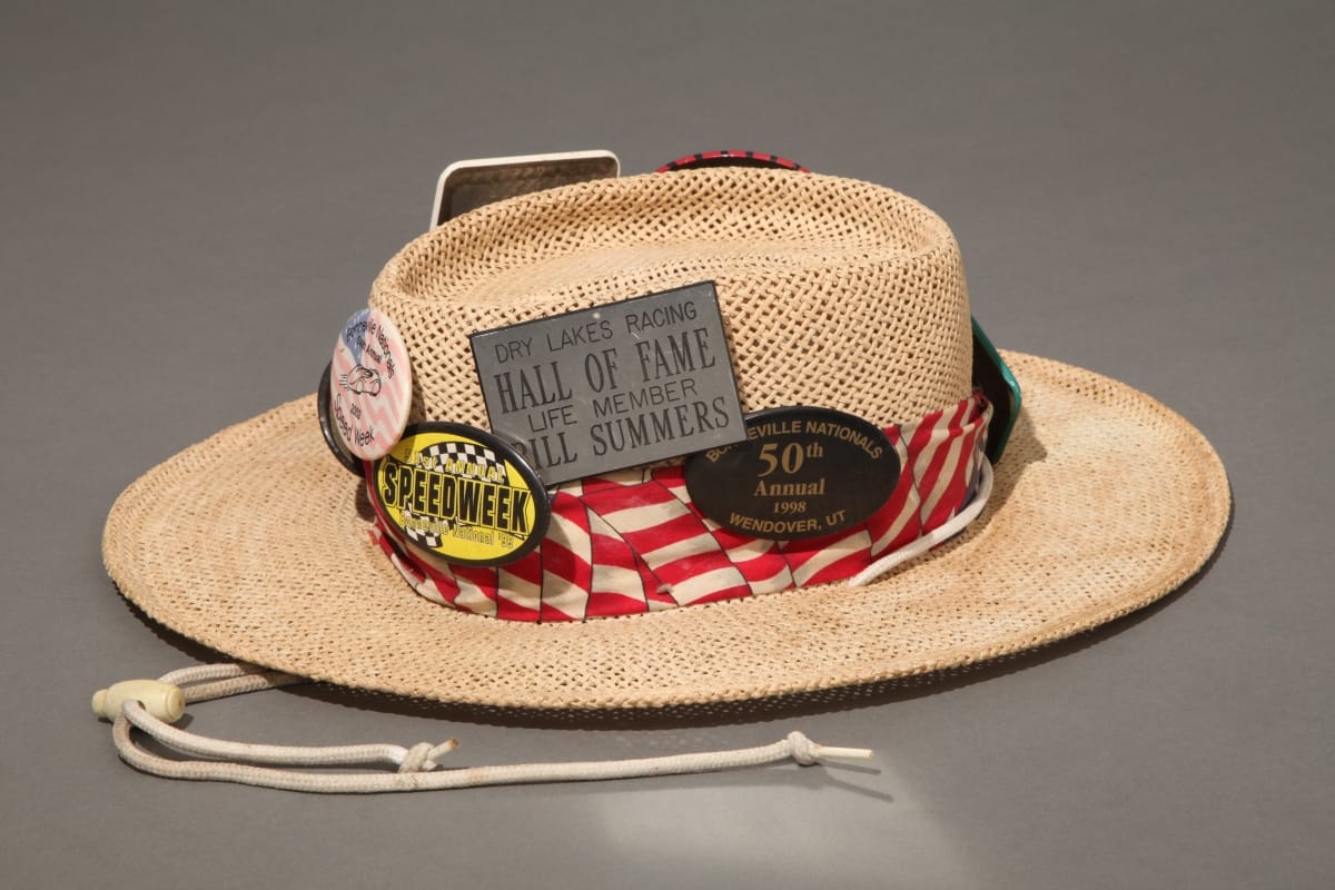 Straw hat with red and white striped band and many buttons and badges containing text and images