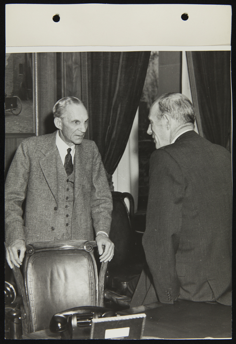 Henry Ford and Lord Halifax Meeting in Henry Ford's Office at the Engineering Laboratory, November 1941 Two men, one holding onto the back of a chair, talk in an office