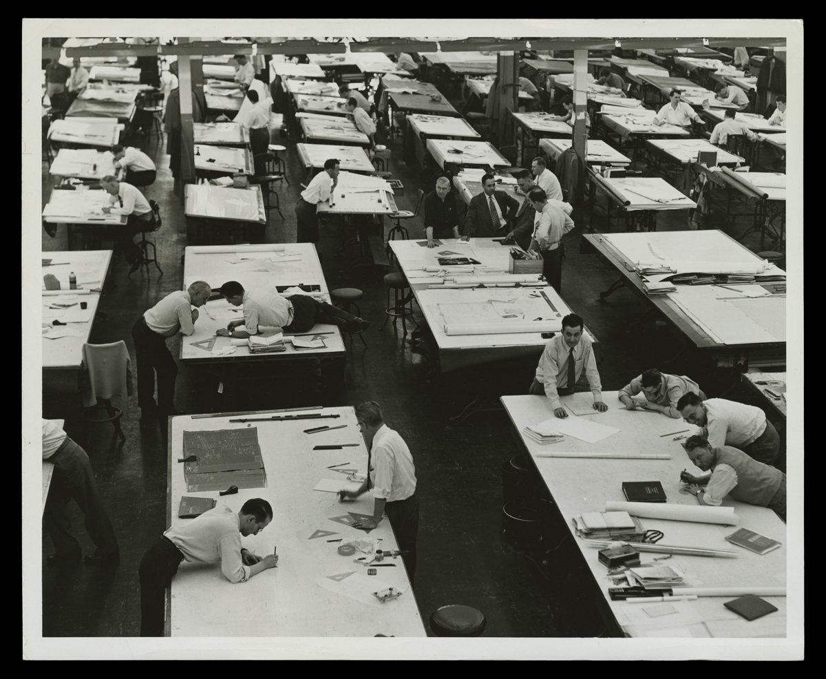 Ford Motor Company Engineering Staff in Main Drafting Room, circa 1952 Large room full of tables, some of which have men standing near, leaning on, or lying on them with pencils or pens in hand