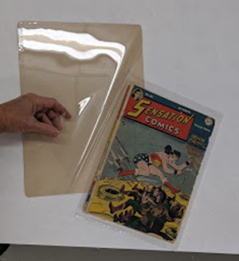 Hand sliding comic book onto a board with plastic over top