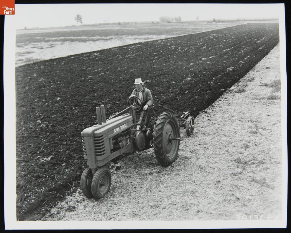 Man Using a 1939-1946 John Deere Model "B" Series Tractor Black-and-white photo of man riding a tractor through a field partially dirt and partially stubble