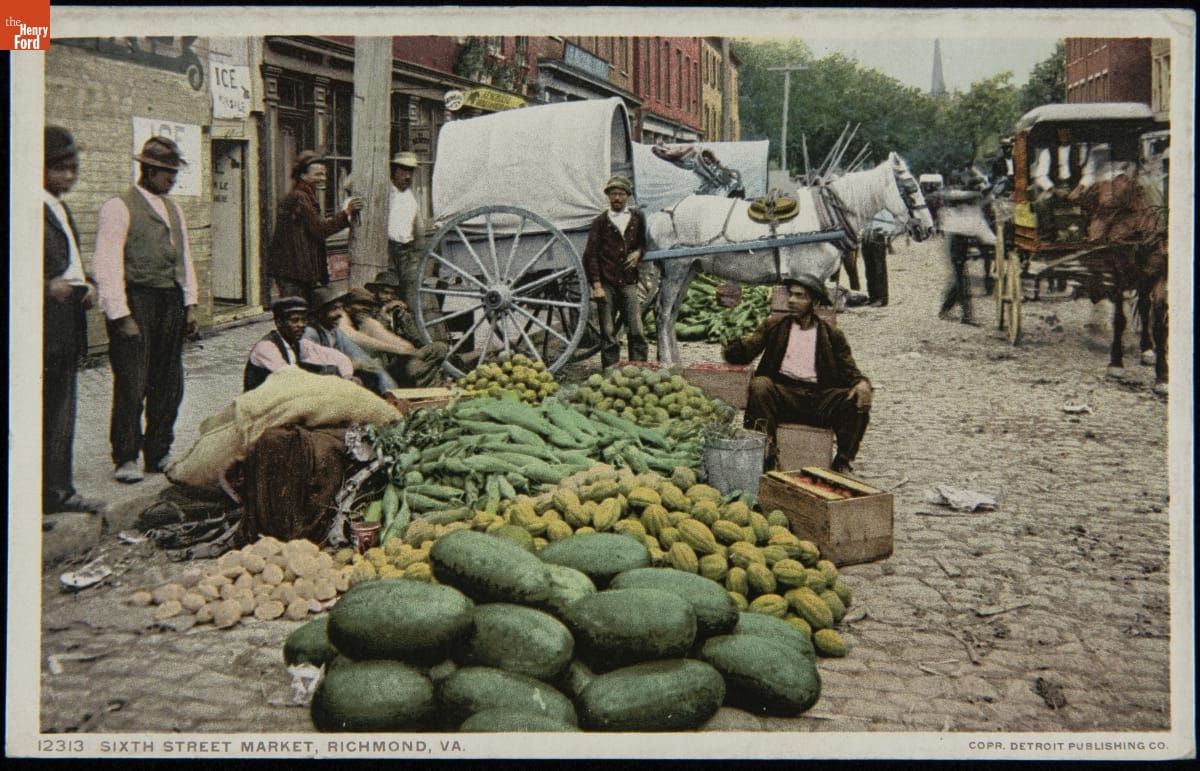 Men sitting and standing by large piles of vegetables at the edge of a street with horses and wagons behind them