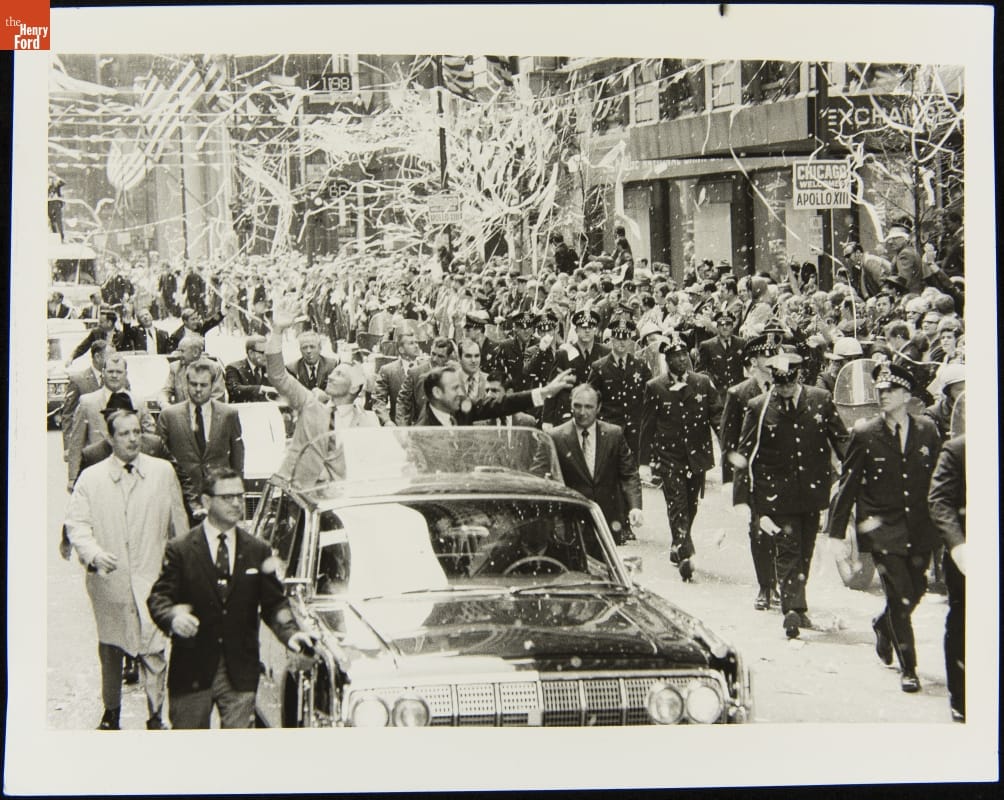 Apollo 13 Astronauts Jack Swigert and Jim Lovell in a Parade, Chicago, Illinois, May 1, 1970 Parade with people standing in an open car, waving; uniformed officers walking alongside; and confetti and tickertape in the air