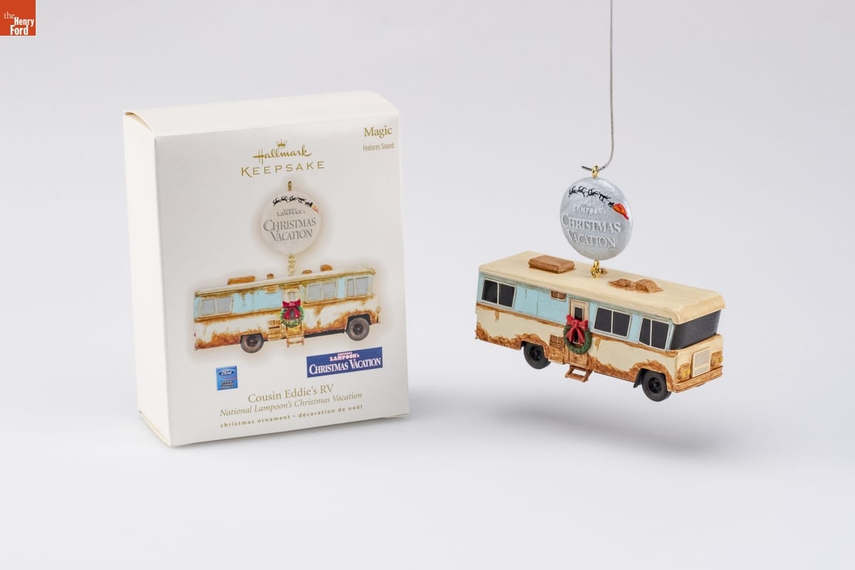 Hallmark "National Lampoon's Christmas Vacation: Cousin Eddie's RV" Christmas Ornament, 2009 Ornament of rusted beige RV with wreath on door, dangling from round silver button reading "National Lampoon's Christmas Vacation," sitting next to a white box with an image of the same ornament on it