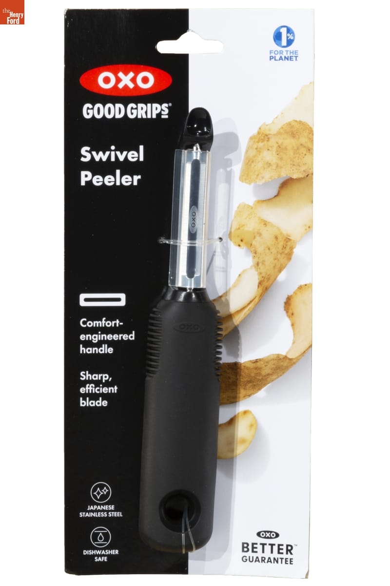 Vegetable peeler with broad black handle in black and white plastic blisterpack with text and image of potato peelings