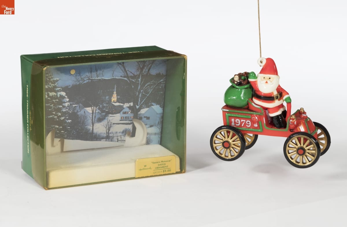 Hallmark "Here Comes Santa Series: Santa's Motorcar" Christmas Ornament, 1979 Ornament of Santa sitting in an old-fashioned open red car with "1979" on side and bag of toys in the backseat; a green box with clear plastic front for the ornament sits next to it