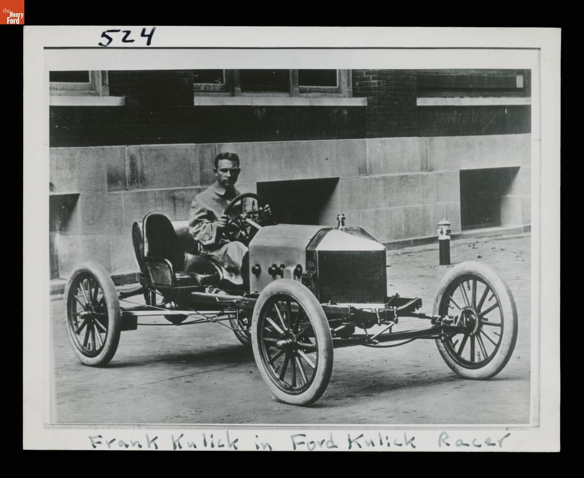 Frank Kulick Sitting in the 1910 Ford Model T Race Car "Kulick Racer" Black-and-white photo of man sitting in early open race car in front of building