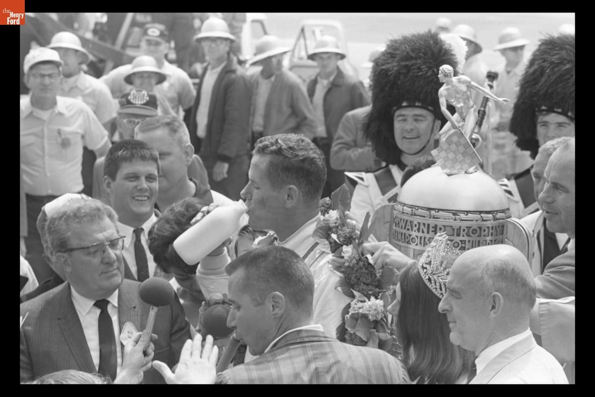 Bobby Unser Drinking Milk after Winning the 52nd Indianapolis 500, May 30, 1968 Man drinks from glass milk bottle in the midst of a crowd with a large trophy and men in beefeater hats nearby