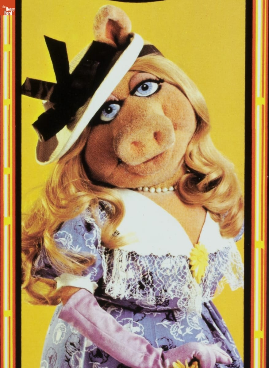 "Jim Henson's Muppets" Lunchbox, 1979 / Miss Piggy detail Pig puppet with blonde wavy hair wearing white hat with black ribbon, elbow-length purple gloves, and a purple dress with white collar