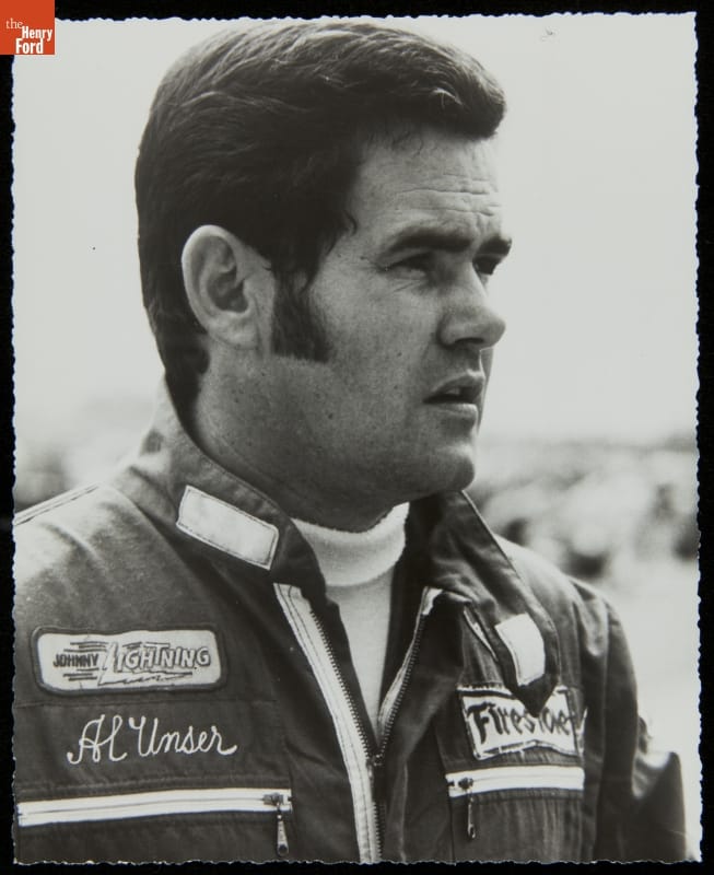 Al Unser, Sr. Black-and-white portrait of man with sideburns wearing jacket or jumpsuit with text and logos