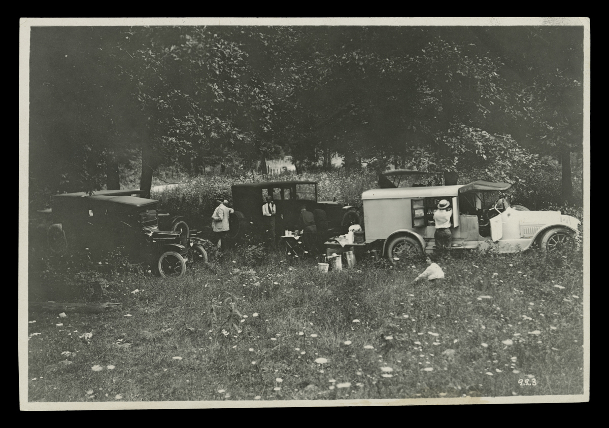 Several cars in a field with people by and near them
