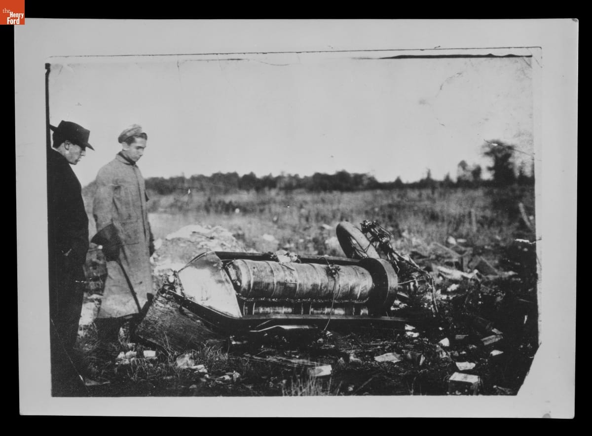 Wreckage of Ford Model K "666" Race Car Driven by Frank Kulick, 1907 Black-and-white photo of two men staring at the crashed remains of a car in a field