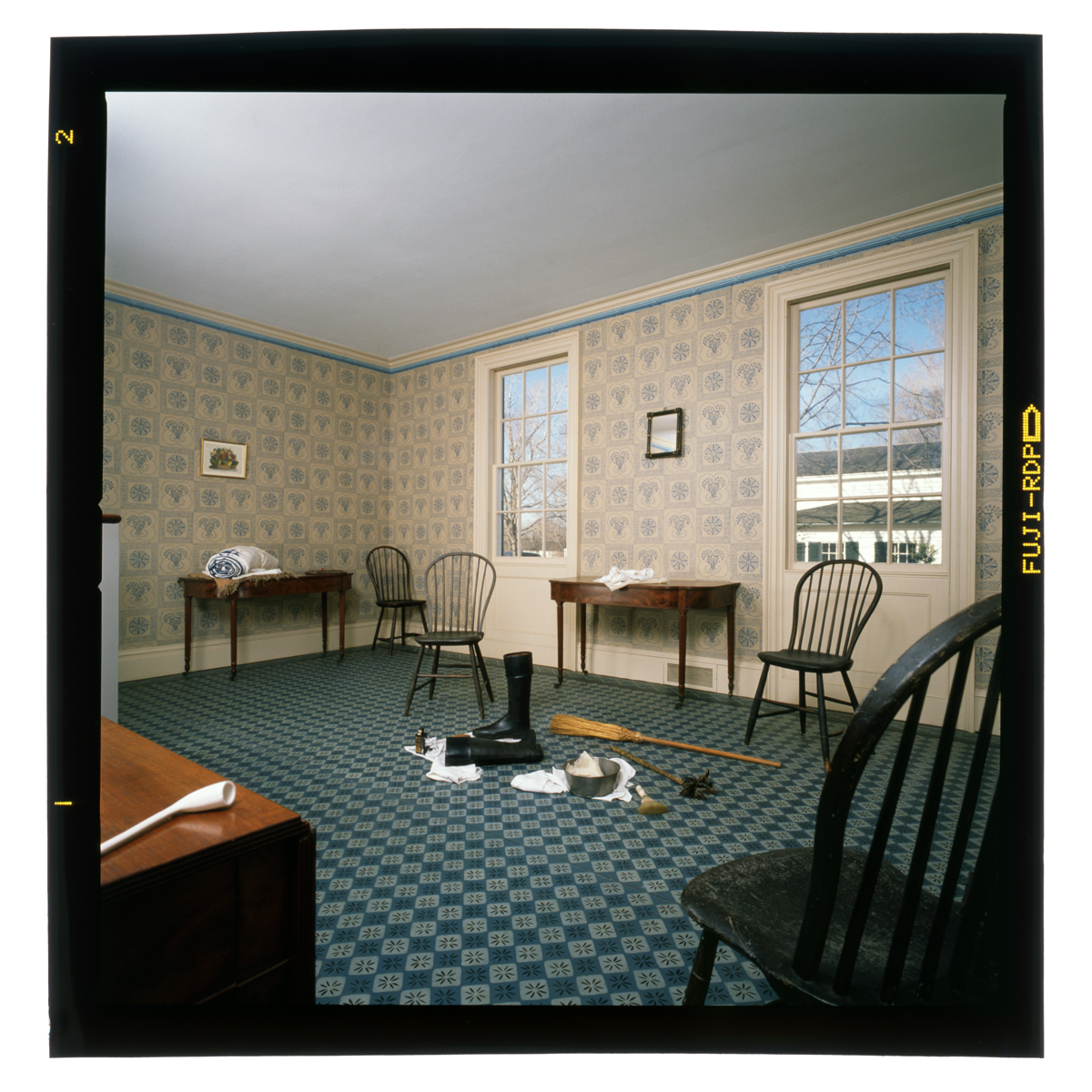 Mostly empty room with patterned floor and wallpaper, containing a few chairs and side tables