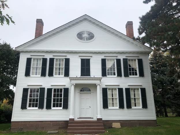 The completed renovation of the façade of the Noah Webster Home Two-story white wooden house with symmetrical windows with black shutters and a peaked roof