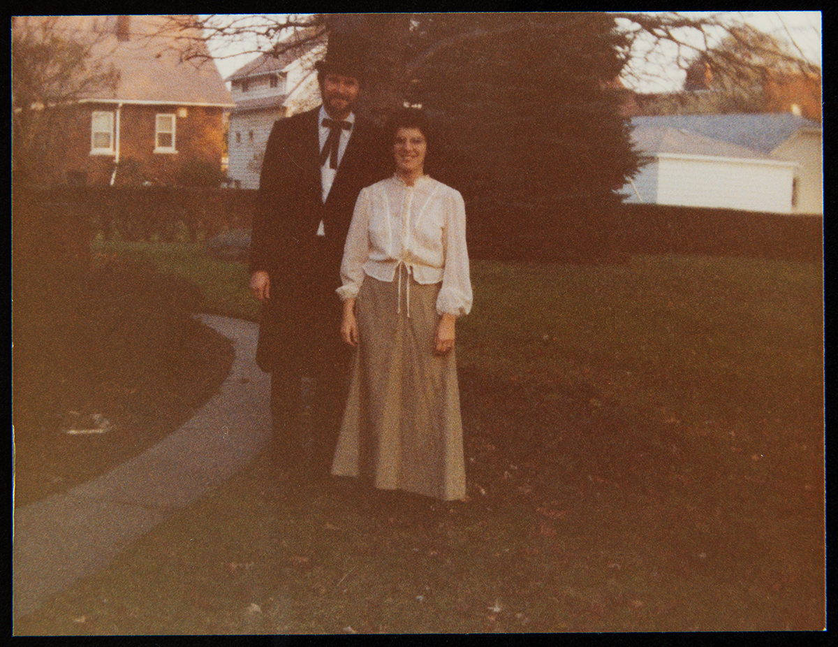 Man and woman standing outside with trees and houses behind them