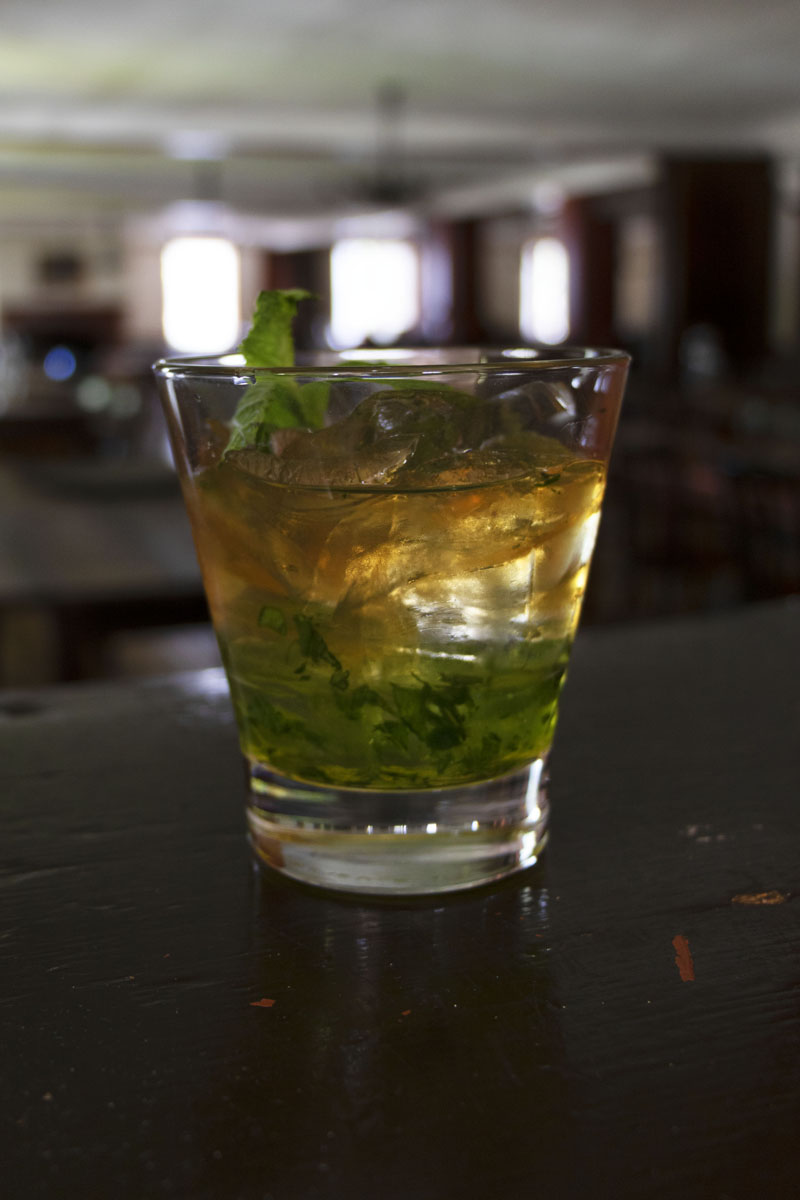 Mint Julep at Eagle Tavern Drink in clear glass with mint leaf on top and muddled mint at bottom of glass; large dining room visible in background