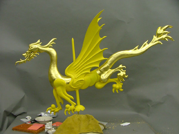 Gilding the dragon weathervane Bright gold, partially shiny and partially dull, figure of dragon with tools and implements nearby