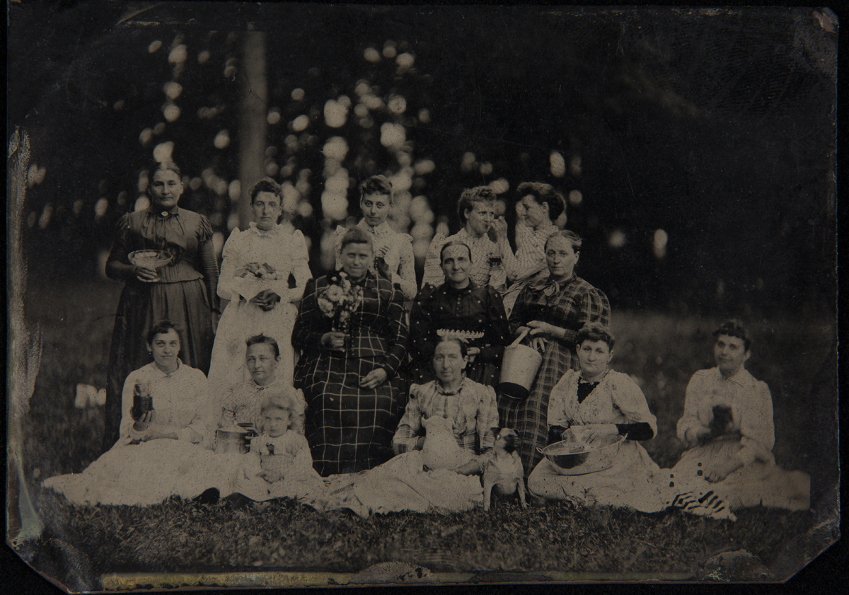Women of various ages posed on a lawn, each holding tableware items